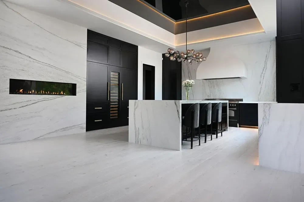 Modern kitchen with white marble, black cabinets, and island with bar stools.