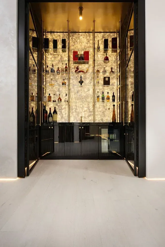 Luxury bar with gold accents, illuminated shelves filled with bottles, and black cabinets.