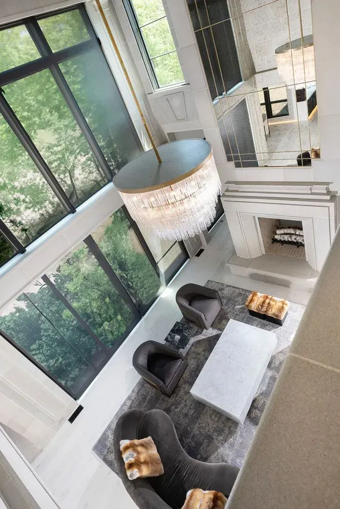High-angle view of a luxury living room with large windows, a chandelier, and modern gray armchairs.
