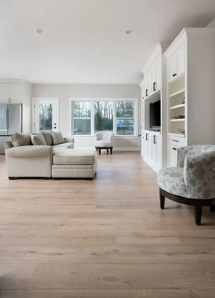 Spacious living room with light wood floors, white cabinetry, and a beige sectional sofa.