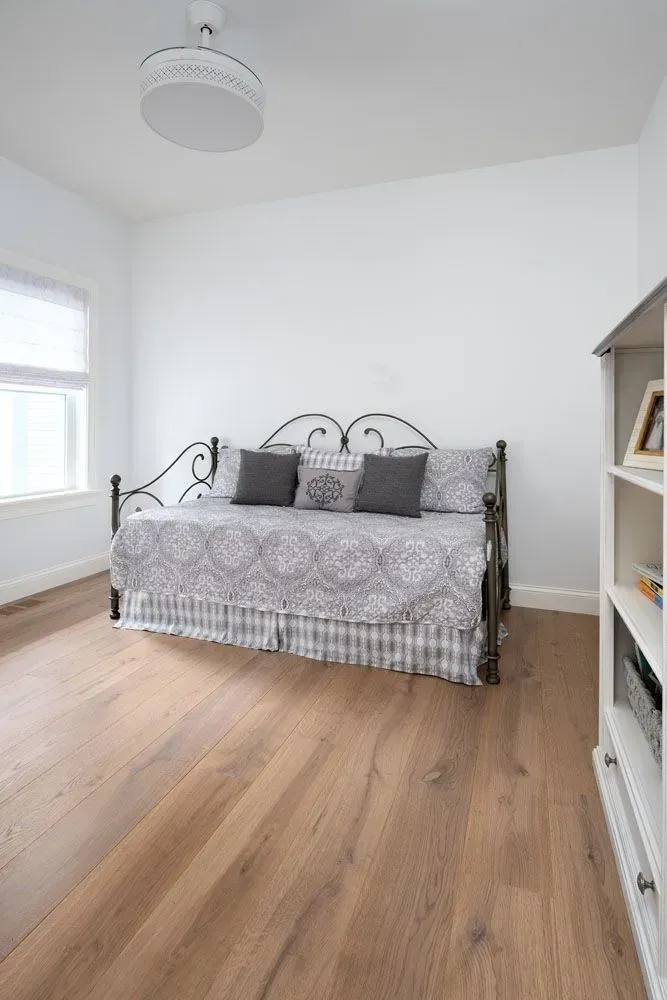Bedroom with daybed, white walls, wooden floor, and bookcase.