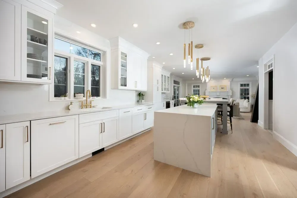Bright white kitchen with island, cabinets, and gold accents. Light wood floor.