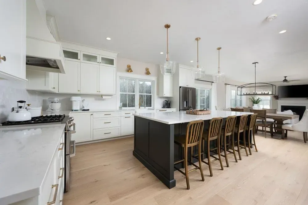 Spacious white kitchen with dark island, bar stools, and dining area in the background.