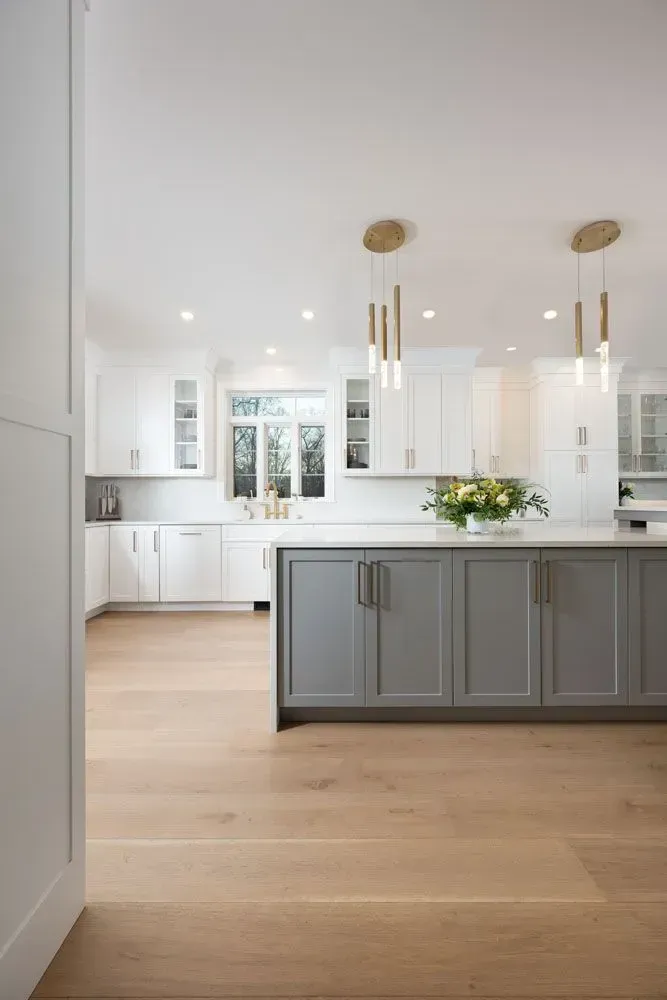 Modern kitchen with gray island, white cabinets, wood floors, and gold pendant lights.