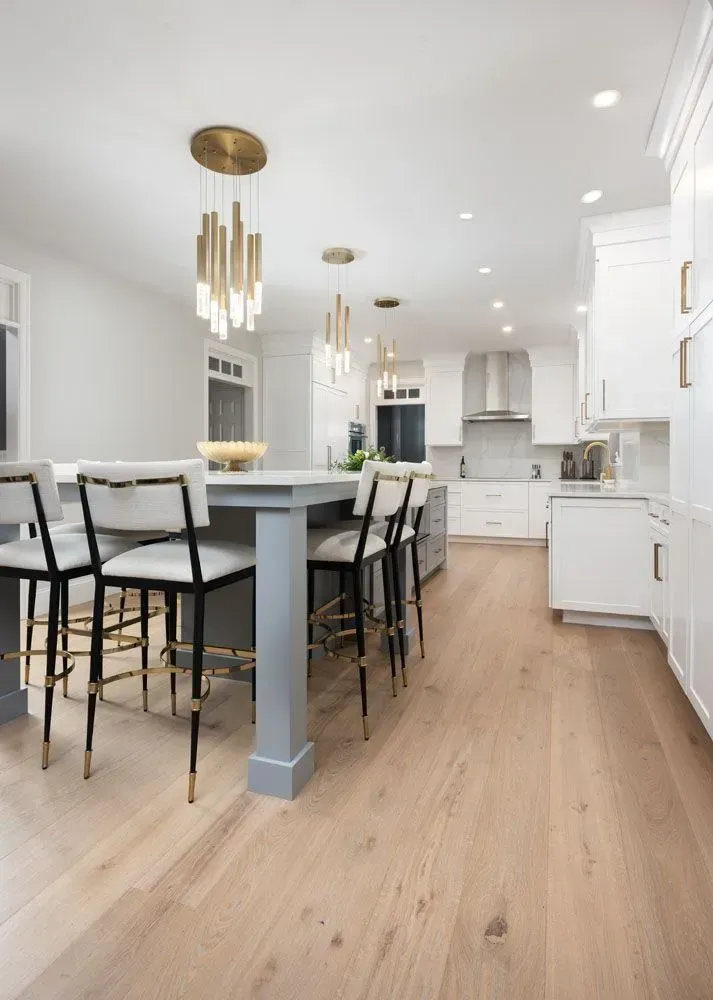 Modern kitchen with gray island, white cabinets, gold accents, and light wood floors.