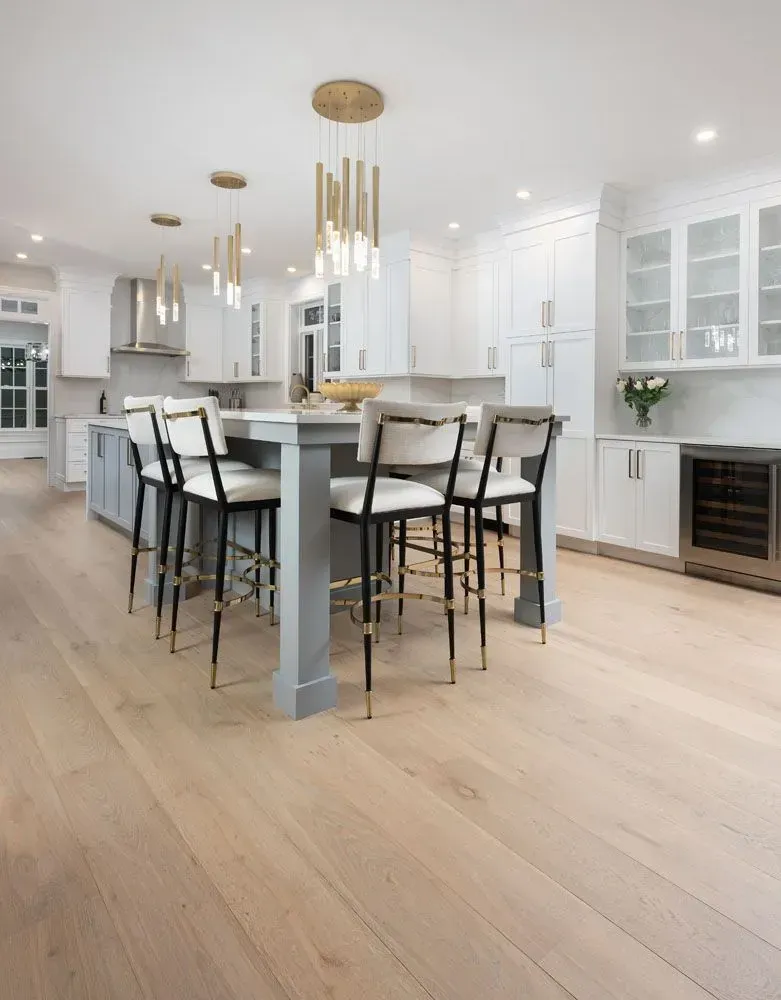 Modern kitchen with a gray island, white cabinets, light wood floors, and gold pendant lights.