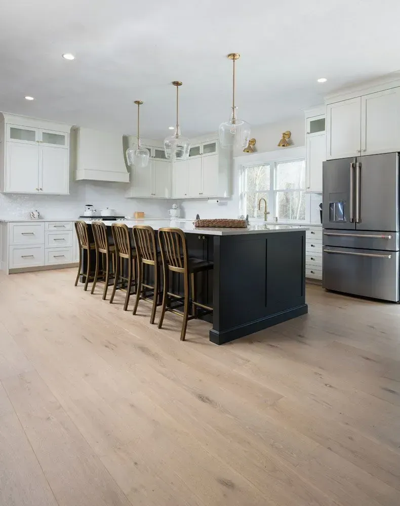 Spacious white kitchen with a dark island, light wood floor, and stainless steel refrigerator.