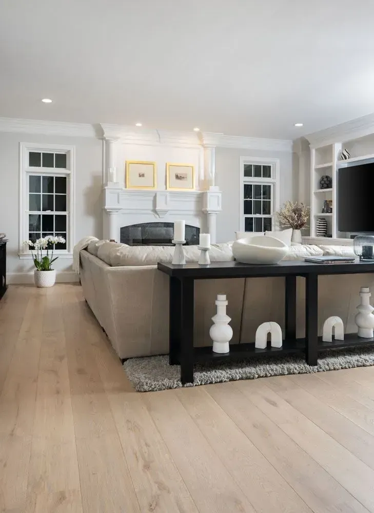 Light-filled living room with light wood floors, neutral walls, fireplace, and black console table with white decor.