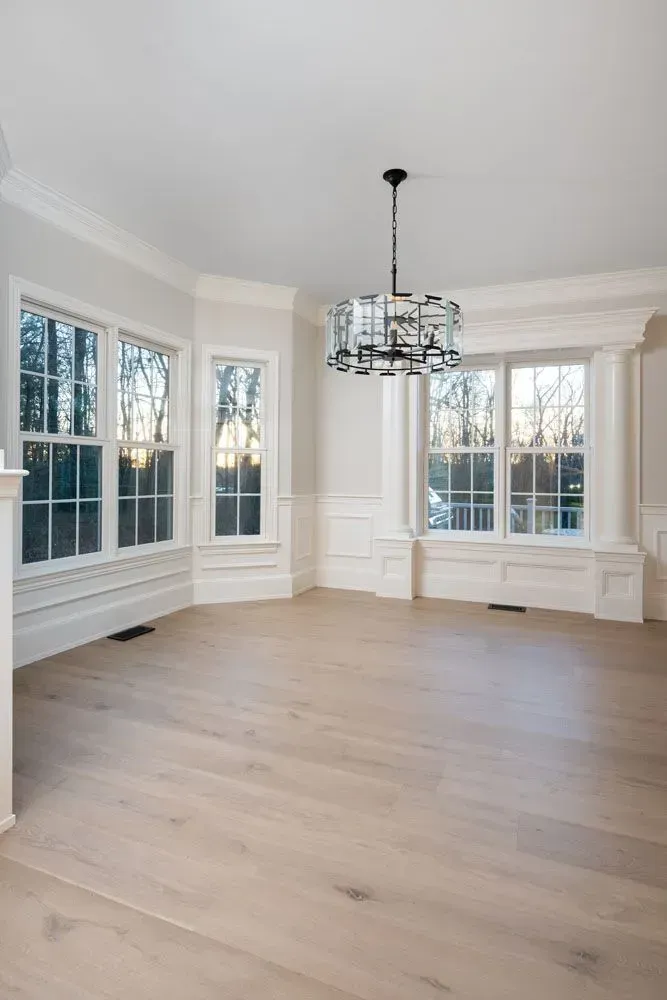 Empty dining room with light wood floor, large windows, and a chandelier.