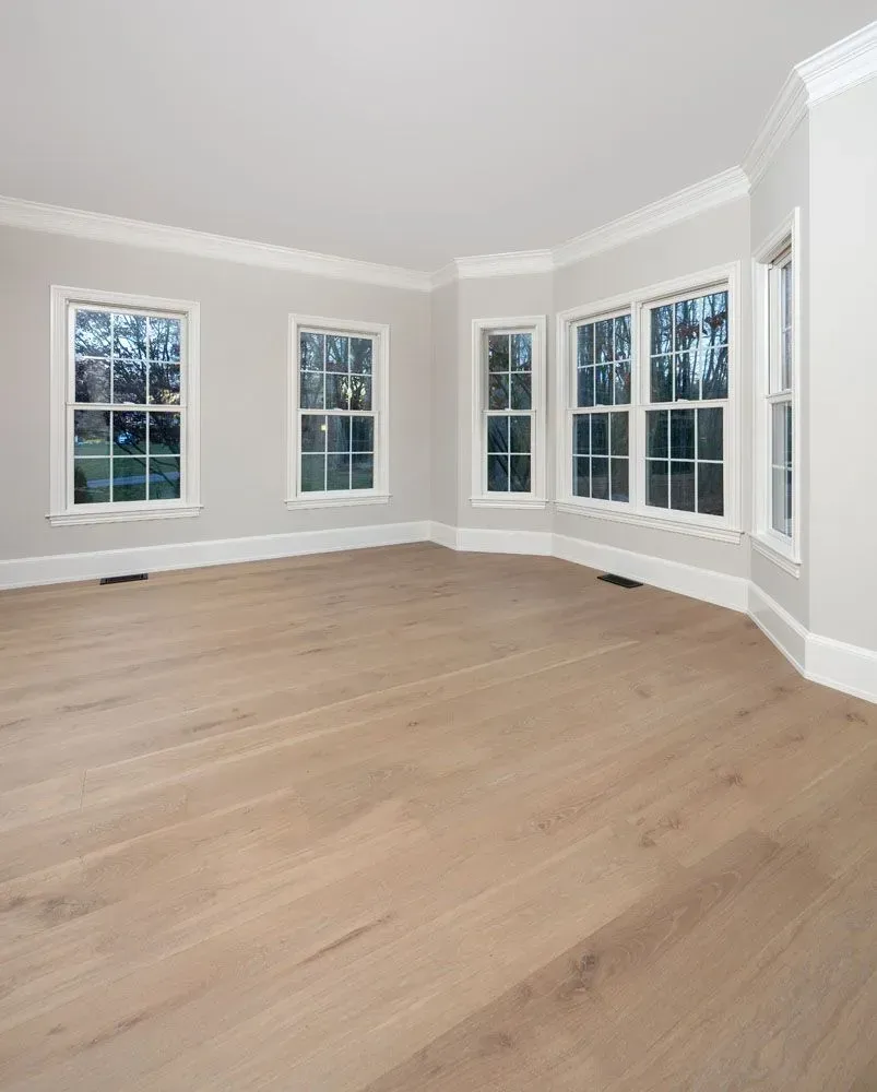 Empty room with light wood floors, multiple windows, and white trim.