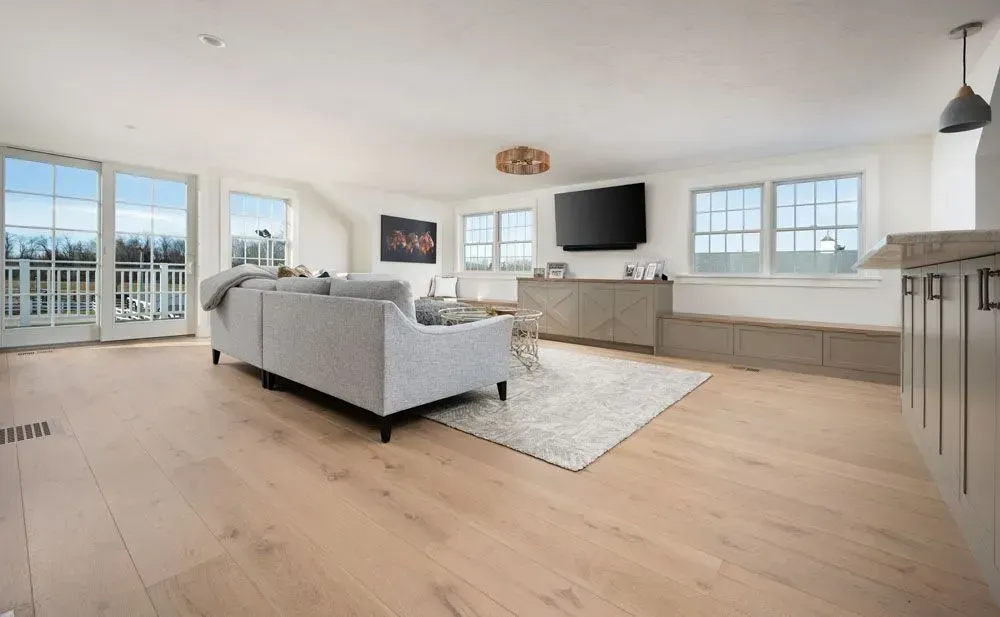 Living room with light wood floors, a gray sofa, and large windows.