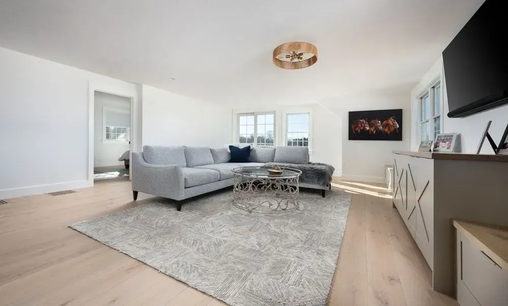 Spacious living room with light gray sectional sofa, area rug, and light wood floors.