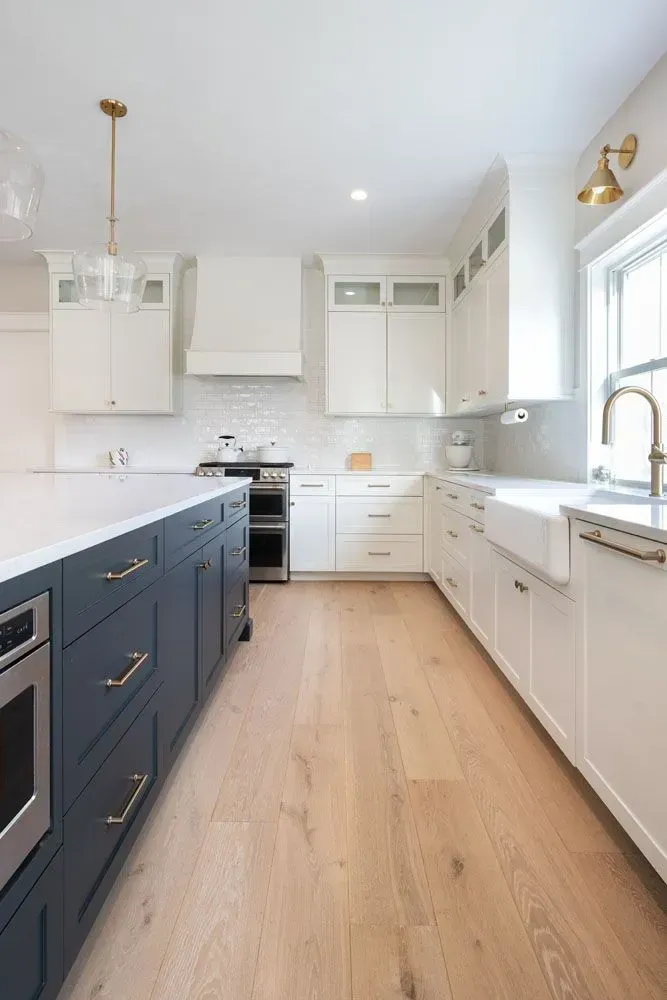 Modern kitchen with blue island, white cabinets, wooden floors, and bright lighting.
