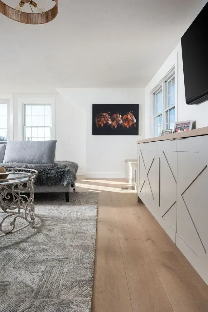 Living room with white walls, light wood floors, and a white cabinet with X-shaped details.