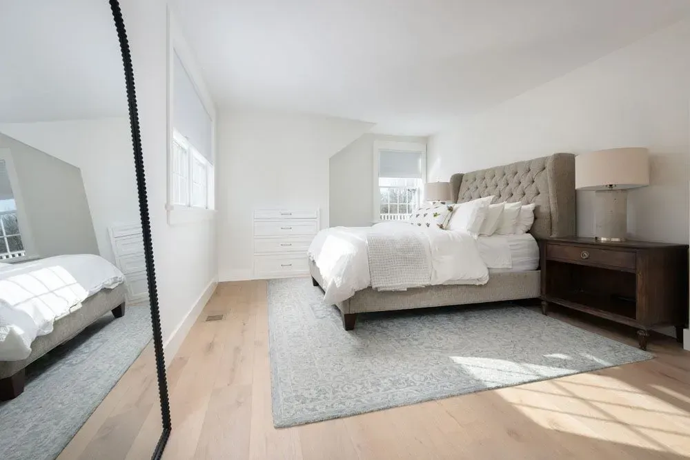 Bright, airy bedroom with a tufted headboard, light wood floors, and a large mirror.