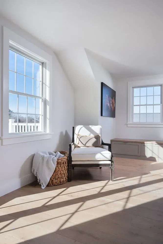 Bright room with chair, basket, and windows casting shadows on wood floor.