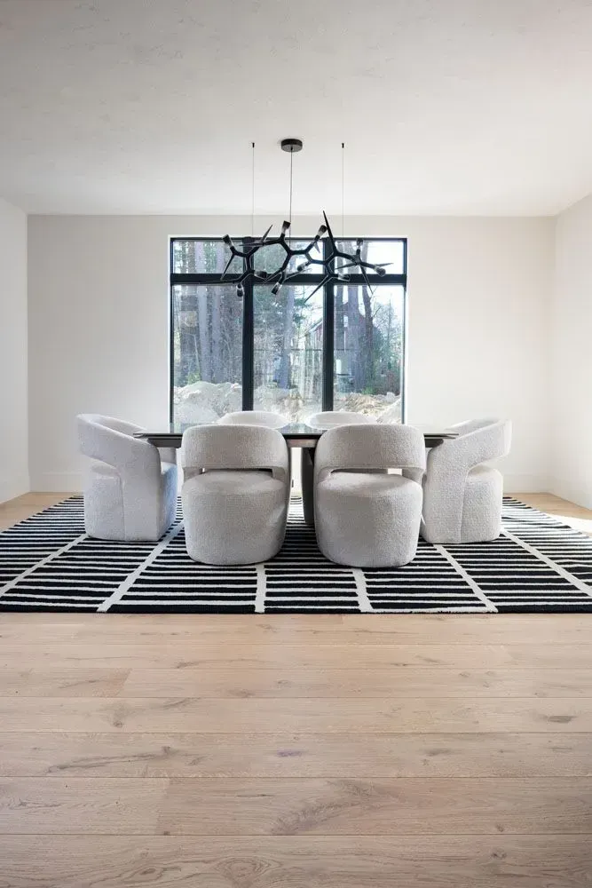 Dining room with a dark table, white chairs, and a black and white rug.