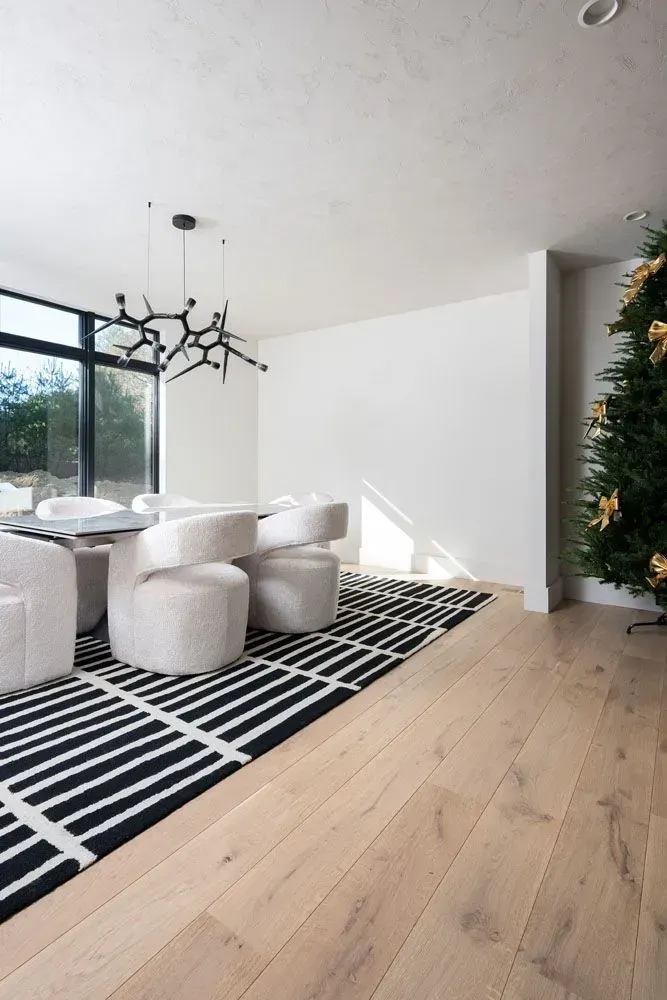 Dining room with a black and white rug, light wood floors, white chairs, and a Christmas tree.