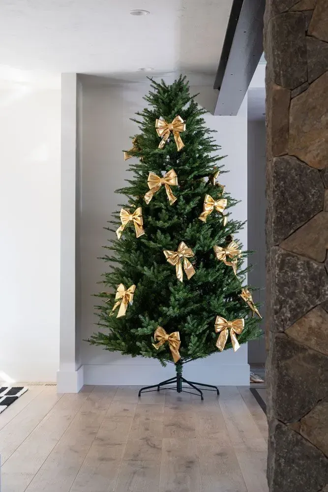 Christmas tree decorated with large gold bows in a bright hallway.