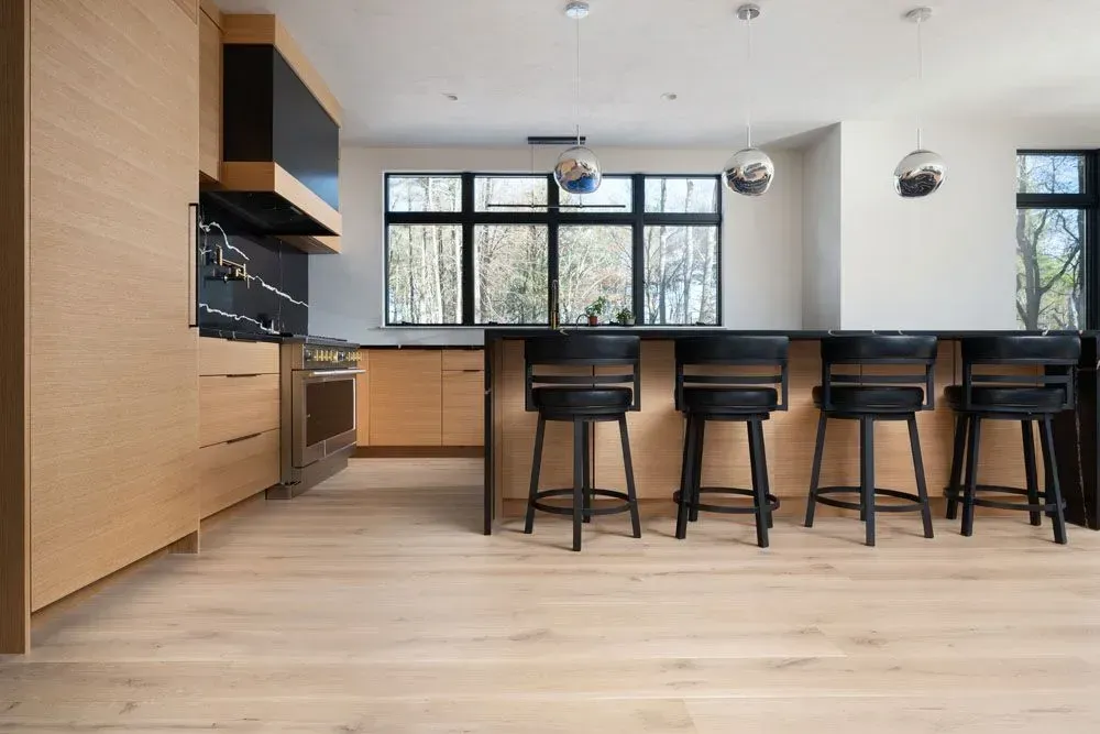 Modern kitchen with light wood cabinets, black island with black stools, and large windows.