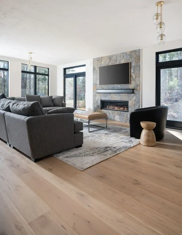 Modern living room with a stone fireplace, grey sofa, and large windows.