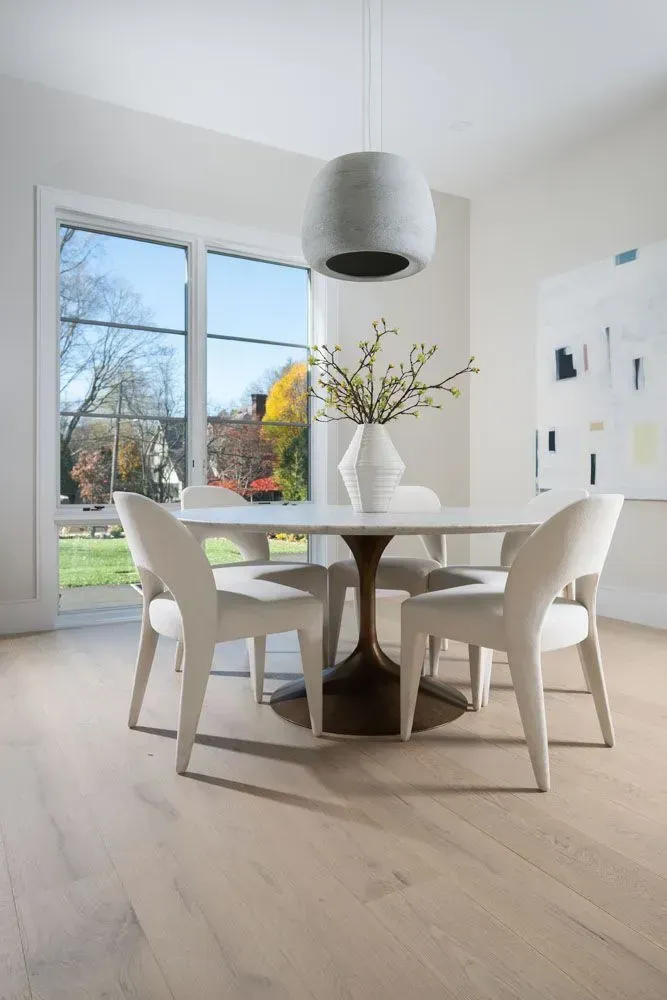 Dining room with round table, four chairs, large window, and modern art.