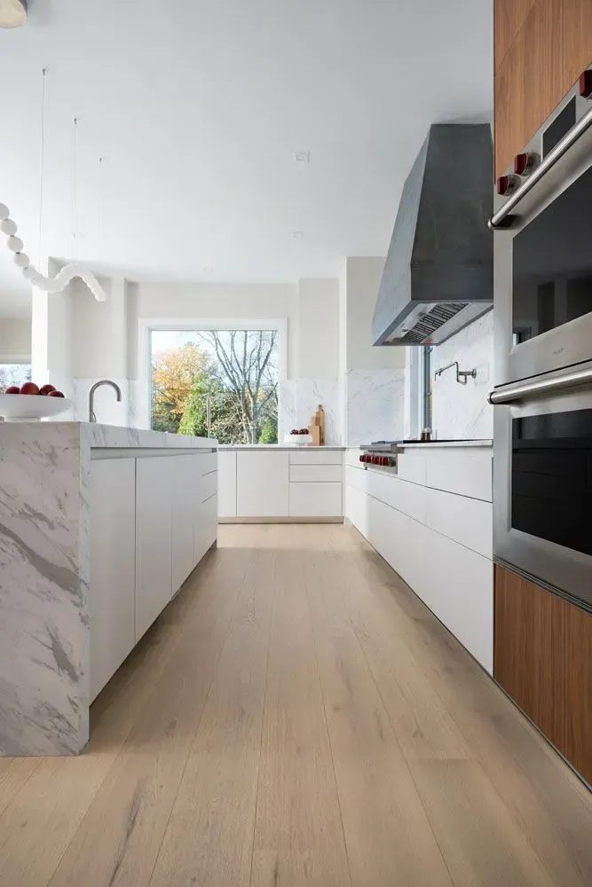 Modern kitchen with white cabinets, marble island, wooden floors, and stainless steel appliances.