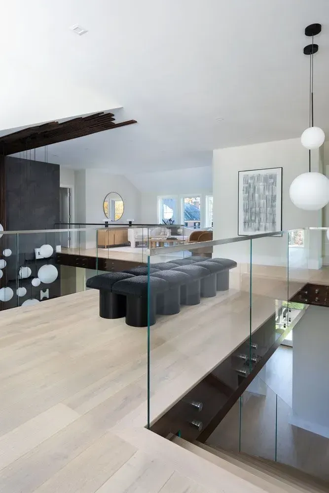 Modern home interior with glass railing, light wood floors, and dark bench.
