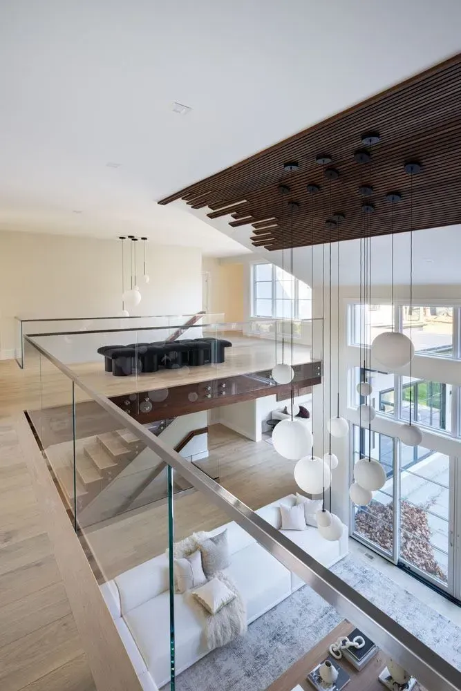 Modern home interior: two-story open space with a piano on a mezzanine, white sofas, large windows.