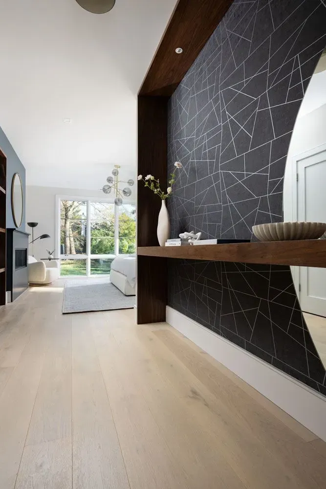 Modern hallway with wood floors, black geometric wallpaper, and a large mirror.
