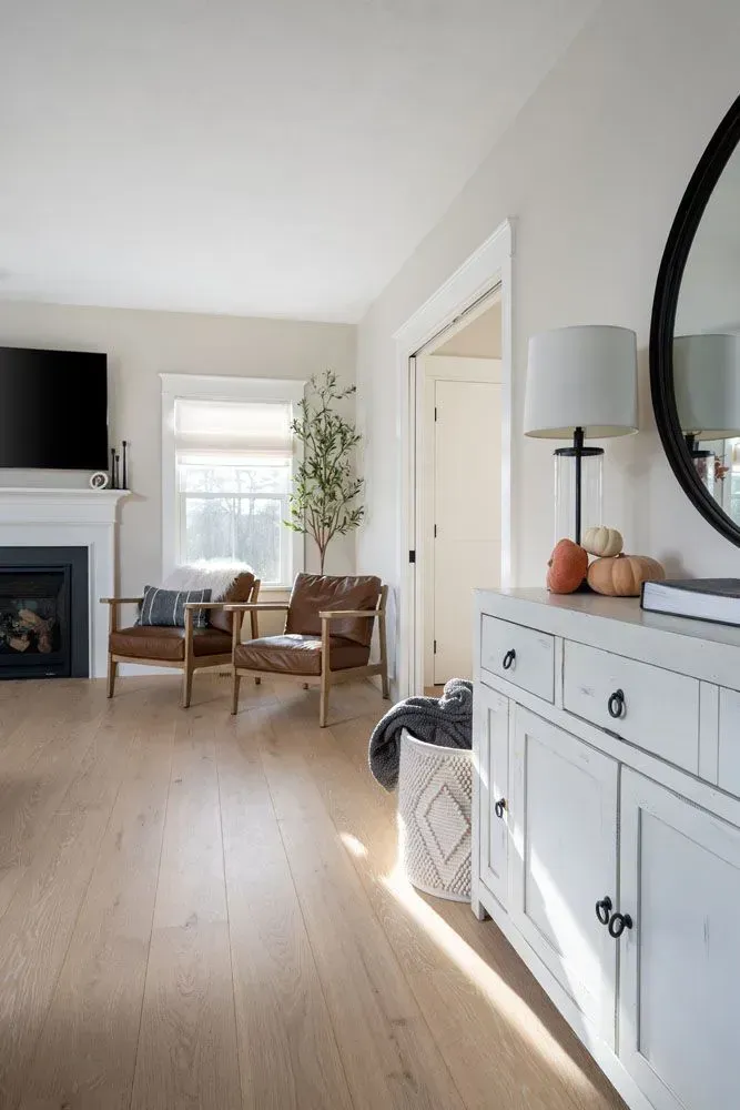 Living room with light wood floors, two leather chairs, white sideboard, and a round mirror.