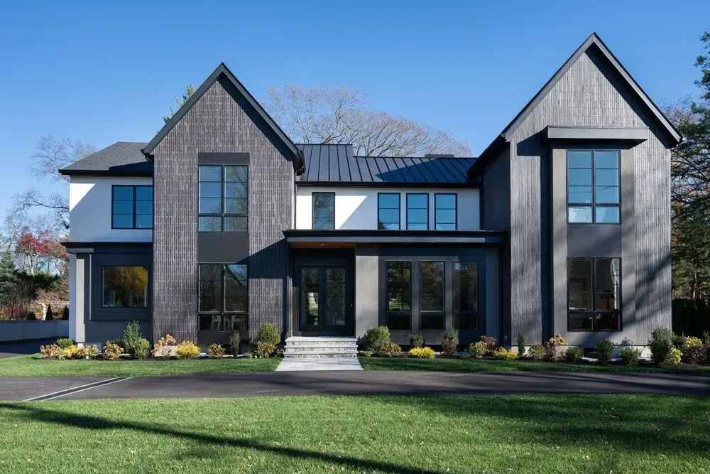 Modern two-story house with black siding, large windows, and a dark metal roof on a sunny day.