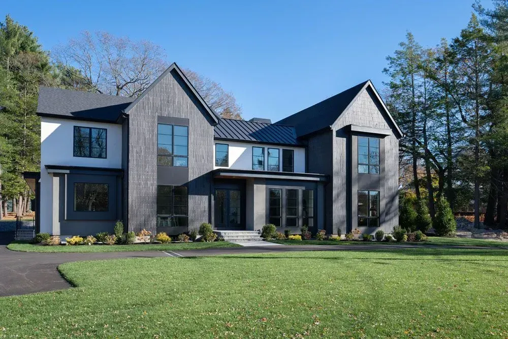Modern two-story house with black siding and white accents; green lawn, trees, and blue sky in background.