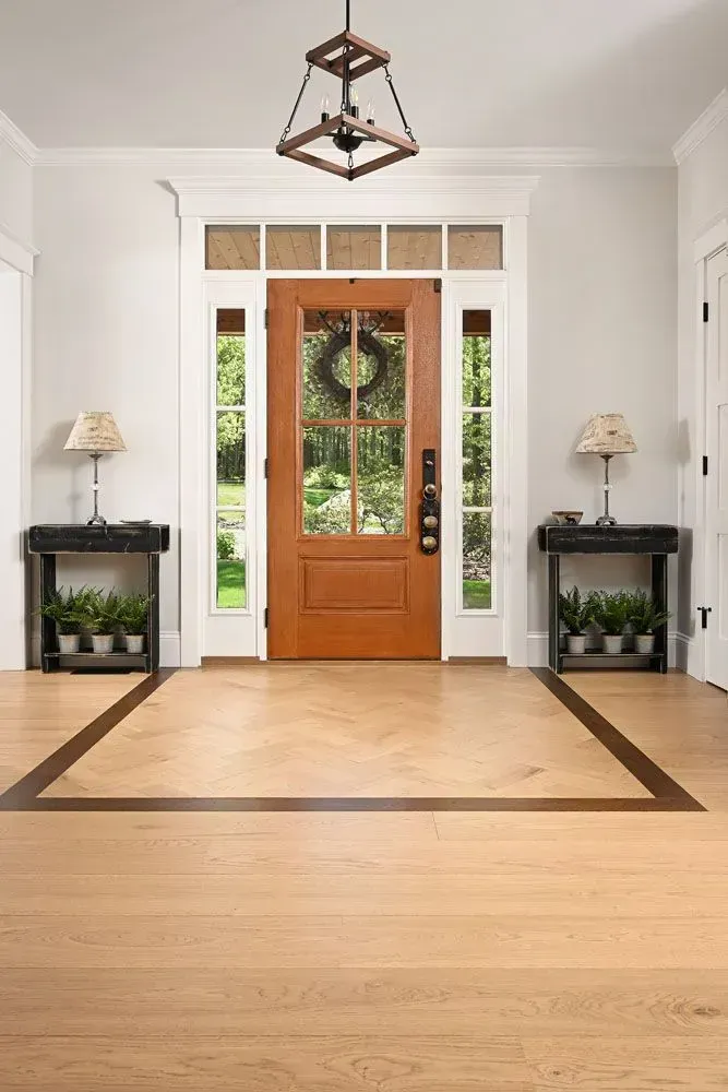 Entryway with wooden door, light-colored flooring, dark framed border, side tables with lamps and plants.