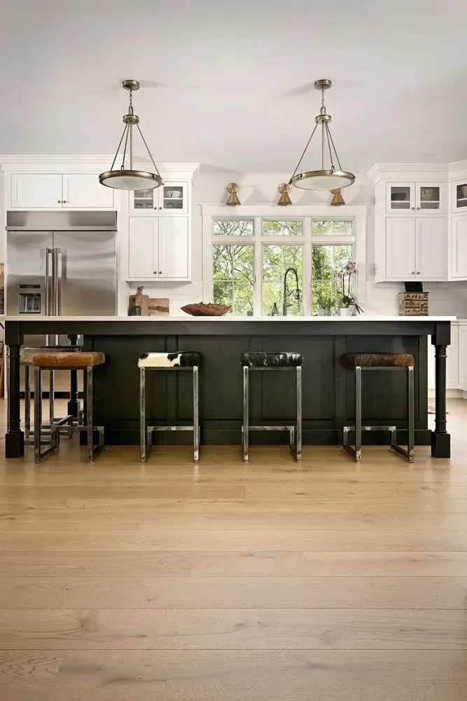 Kitchen with black island, white cabinets, wood floors, and chrome bar stools.