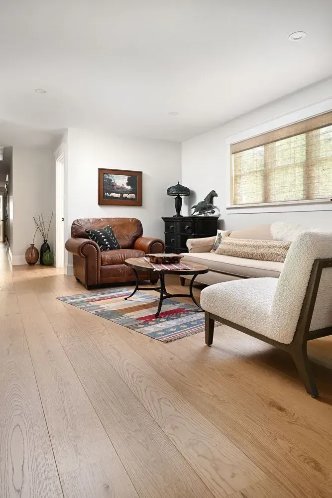 Living room with leather armchair, rug, beige sofa, light wood floor, and a window.