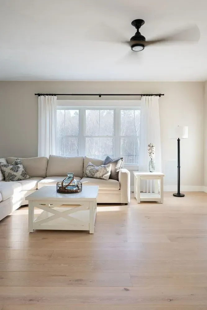 Living room with a white sectional sofa, wooden floors, and a large window with sheer curtains.