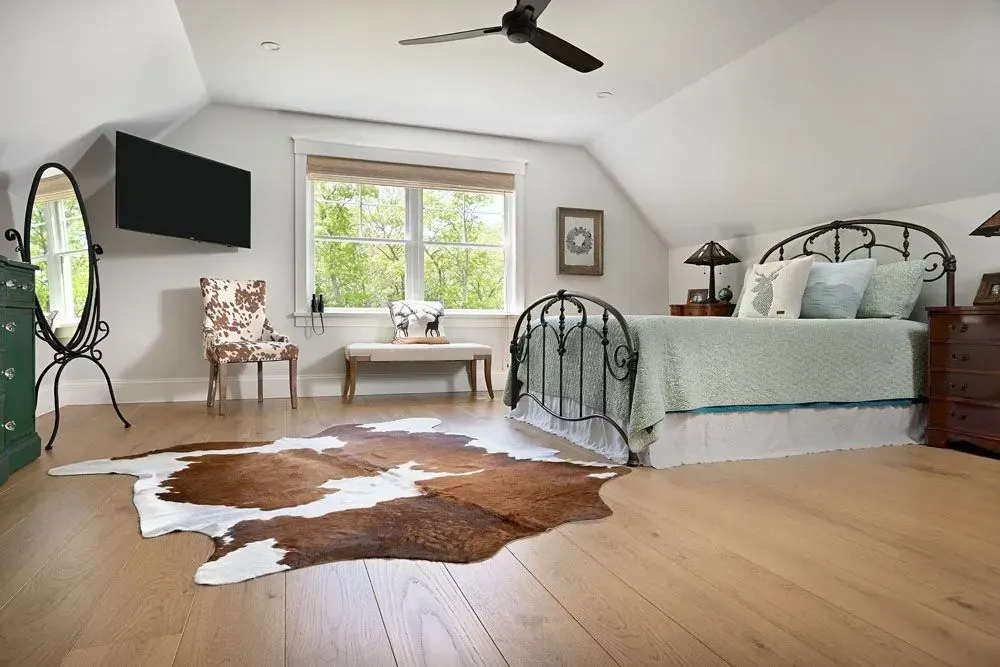 Bedroom with cowhide rug, black bedframe, TV, chair, and window with natural light.