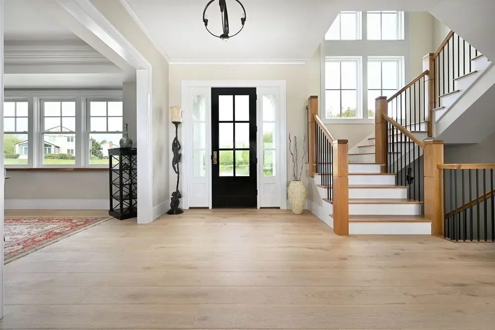 Bright foyer with wooden floors, staircase, and black door.