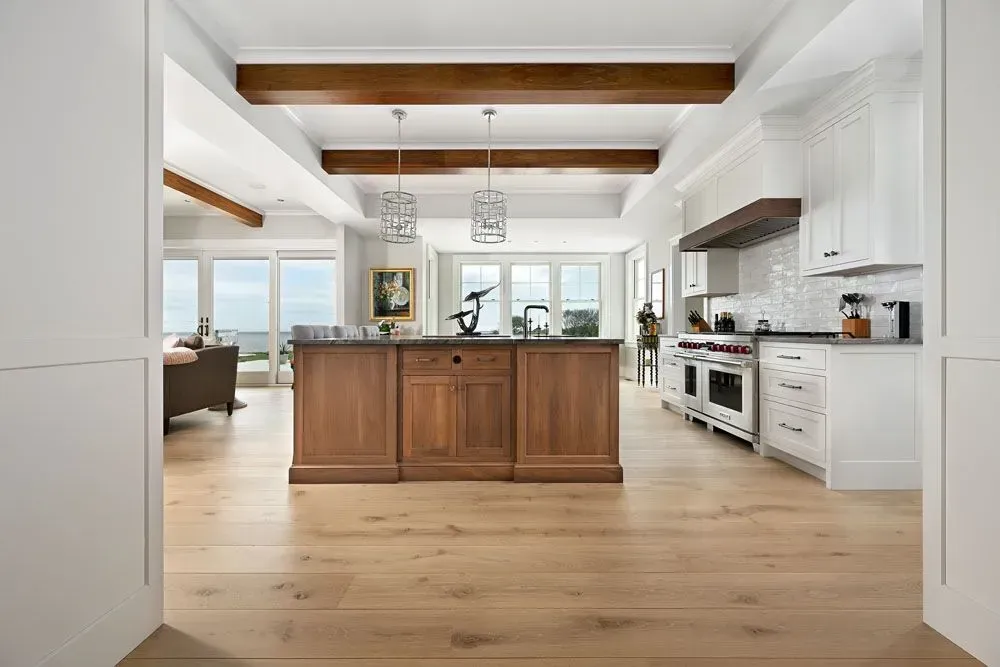 Spacious kitchen with wood island and white cabinets, framed by a light wood floor and exposed wooden beams.