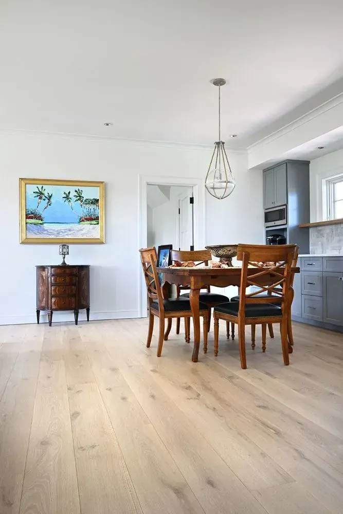 Dining room with wooden table and chairs, light wood floors, and a painting on the wall.