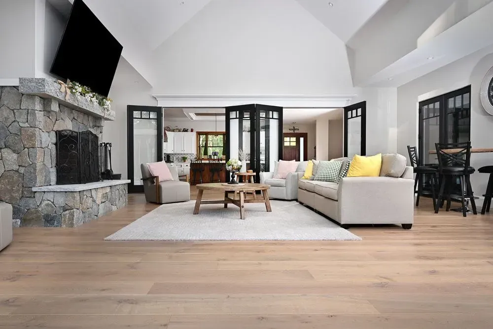 Spacious living room with light wood floors, stone fireplace, white walls, and a cozy seating area.