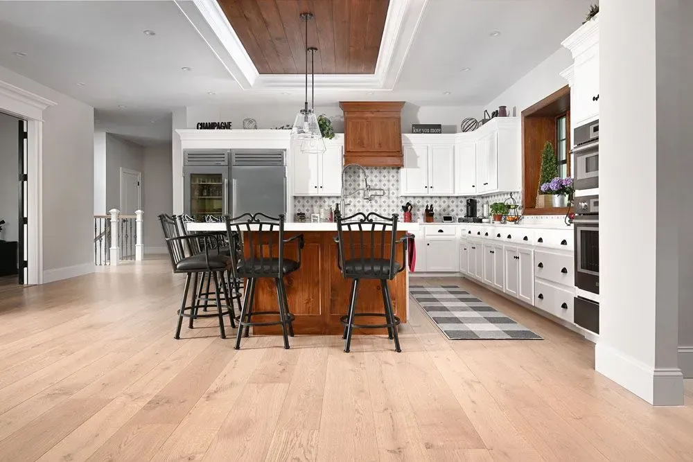 Kitchen with light wood floors, white cabinets, and a dark wood island with black chairs.