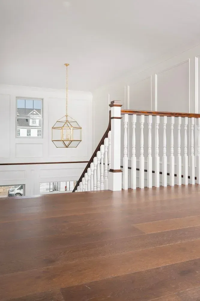 Wooden staircase with white balustrade, gold pendant light, and a small window.