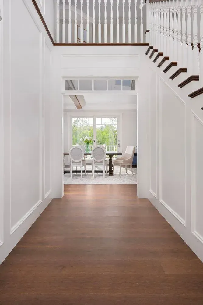 Hallway with dark wood floor leading to dining room with white chairs and table. Staircase on right.