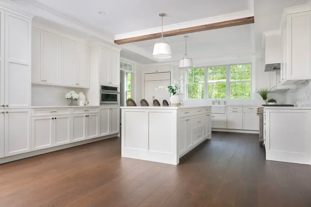White kitchen with island, wood floors, and large windows; bright and airy.