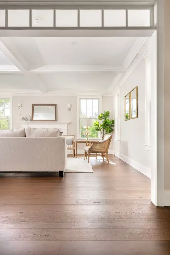 Living room with dark wood floors, white walls, and neutral furniture; bright, natural light.