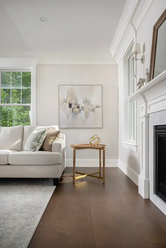 Living room with white sofa, artwork, and fireplace. Dark wood floor, neutral walls.