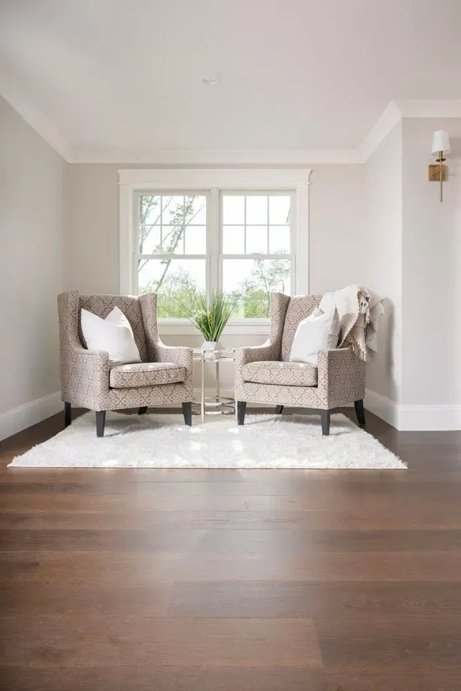 Two patterned wingback chairs face a window, with a small table between them, on a white rug.