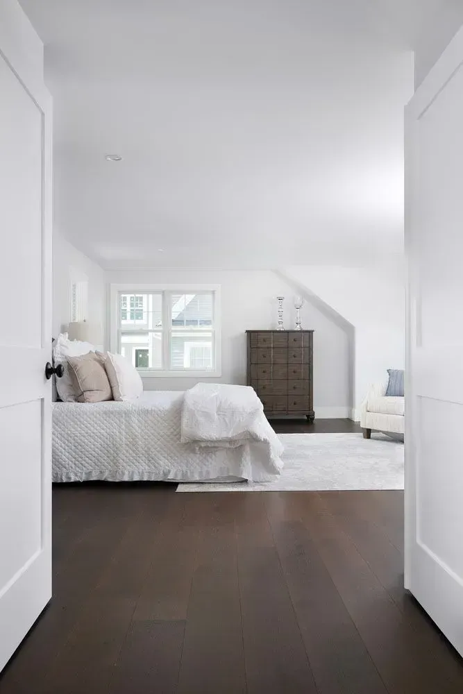 Bedroom interior with dark wood floor, white walls, and a bed with neutral bedding.